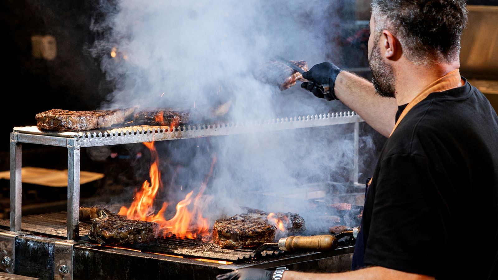 Chef grilling steaks over a flame